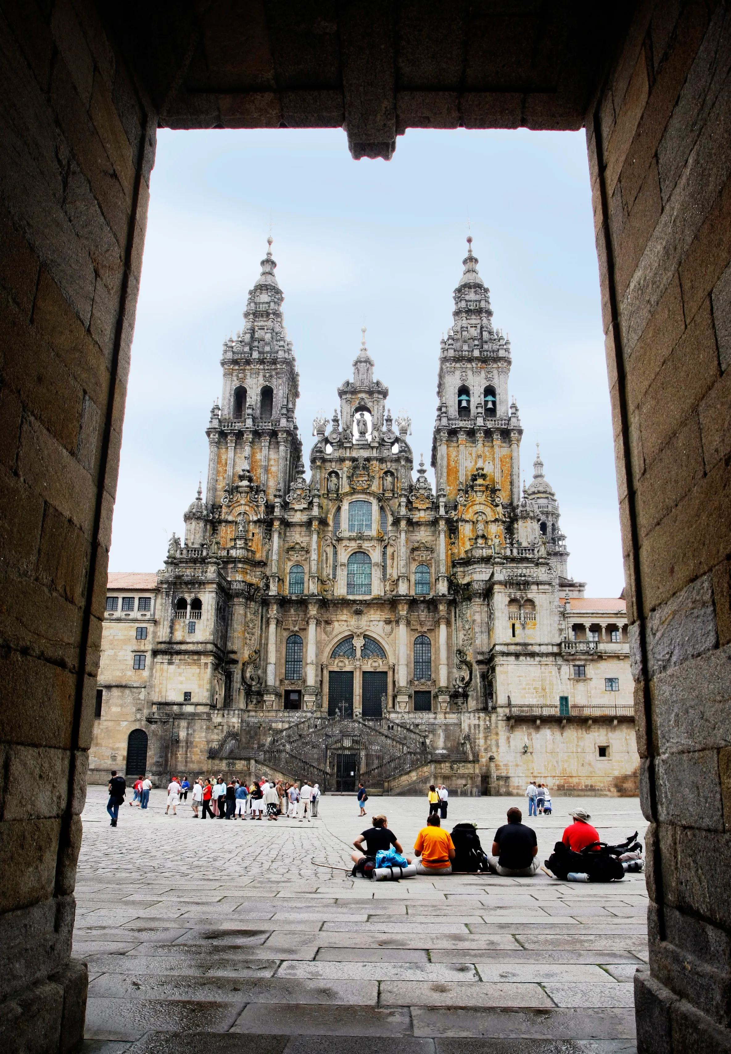 Pilgrims resting beneath an archway with Santiago Cathedral directly ahead.
