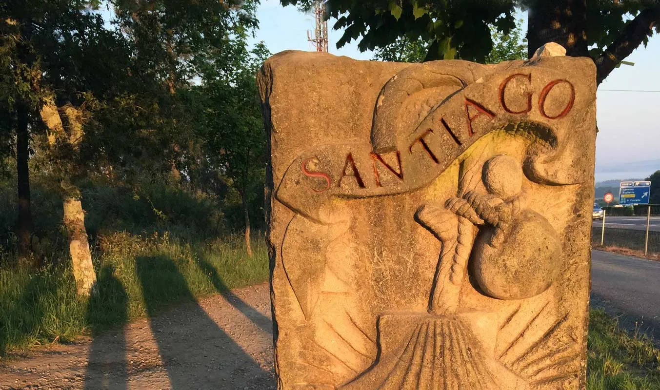 A Camino distance marker beside an open path toward Santiago.