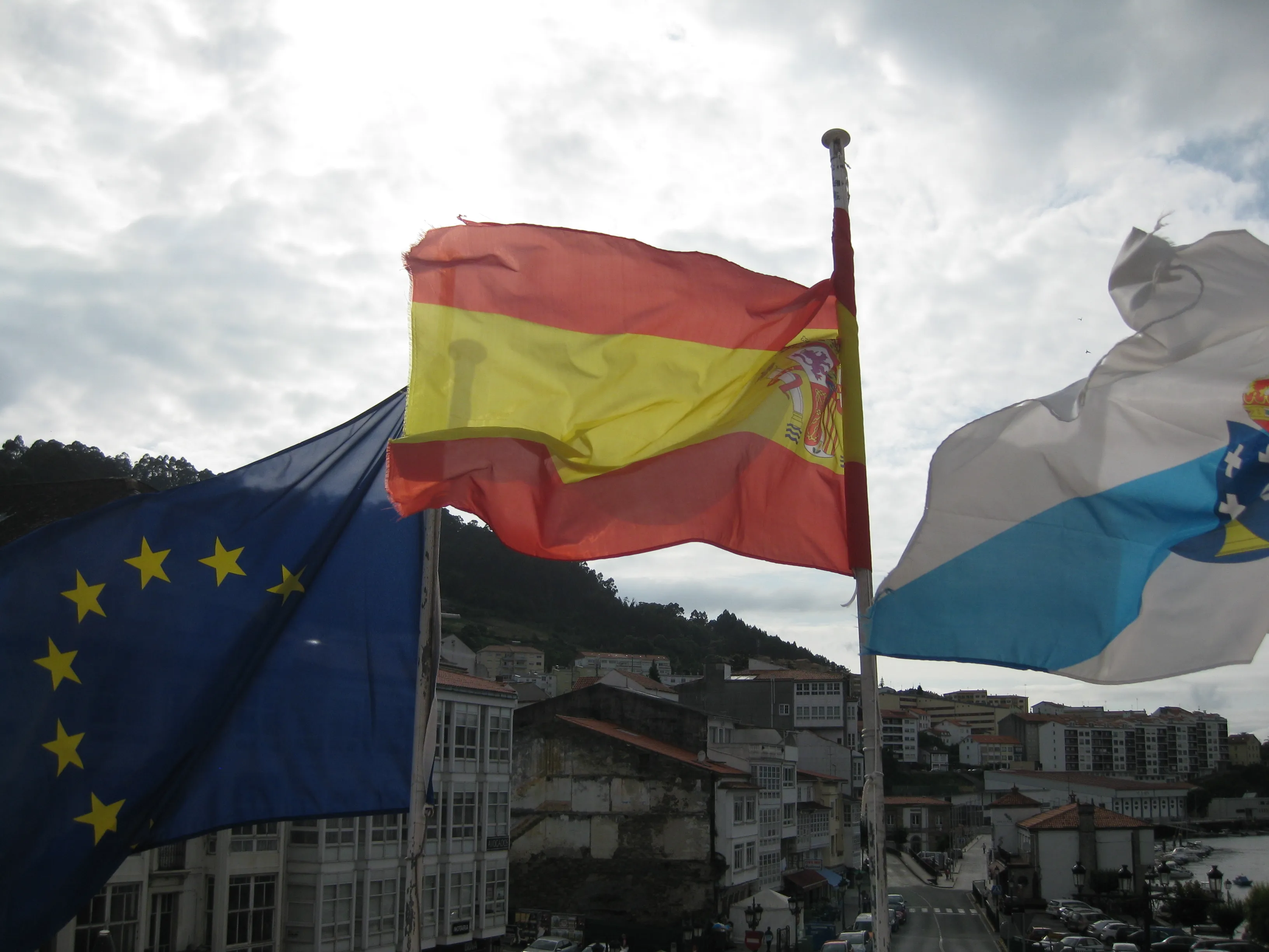 The flags of the European Union, Spain and Galicia flying over a Galician town.
