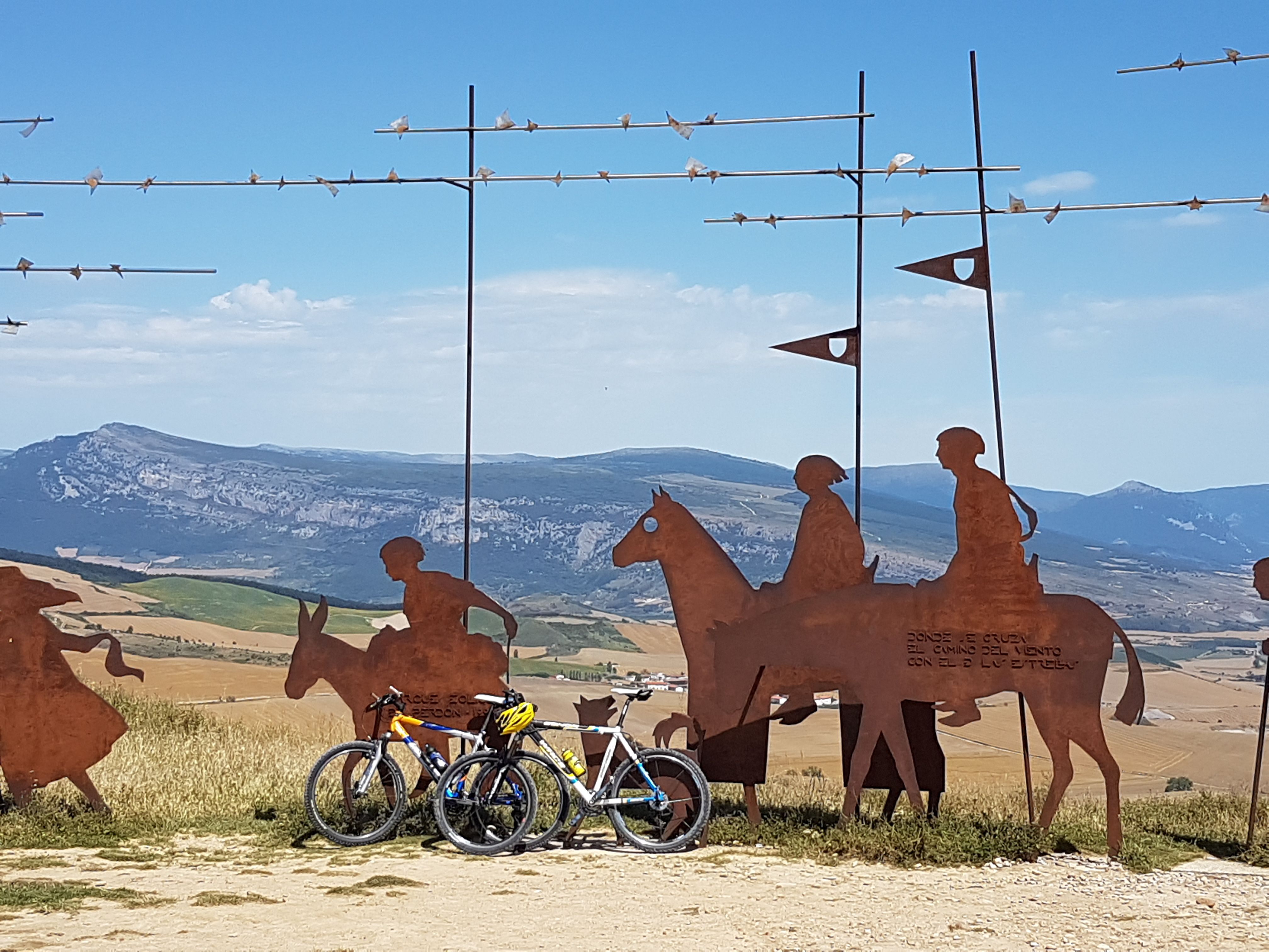 Pilgrim figures and bicycles overlooking the French Way landscape.
