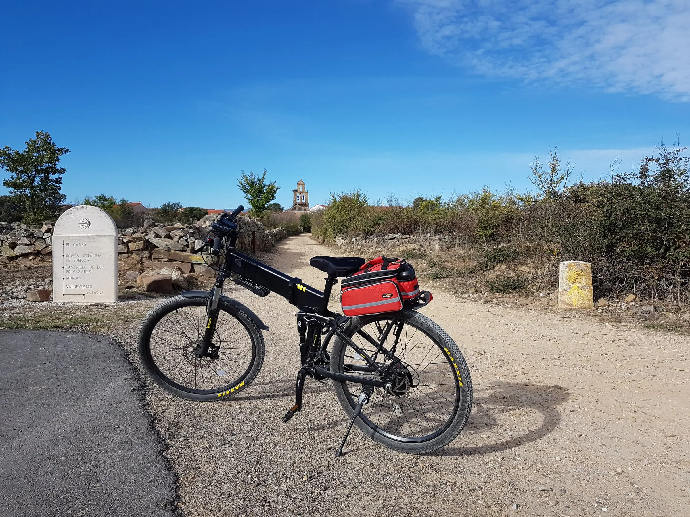 A touring bicycle beside a Camino marker and stone church on the French Way.