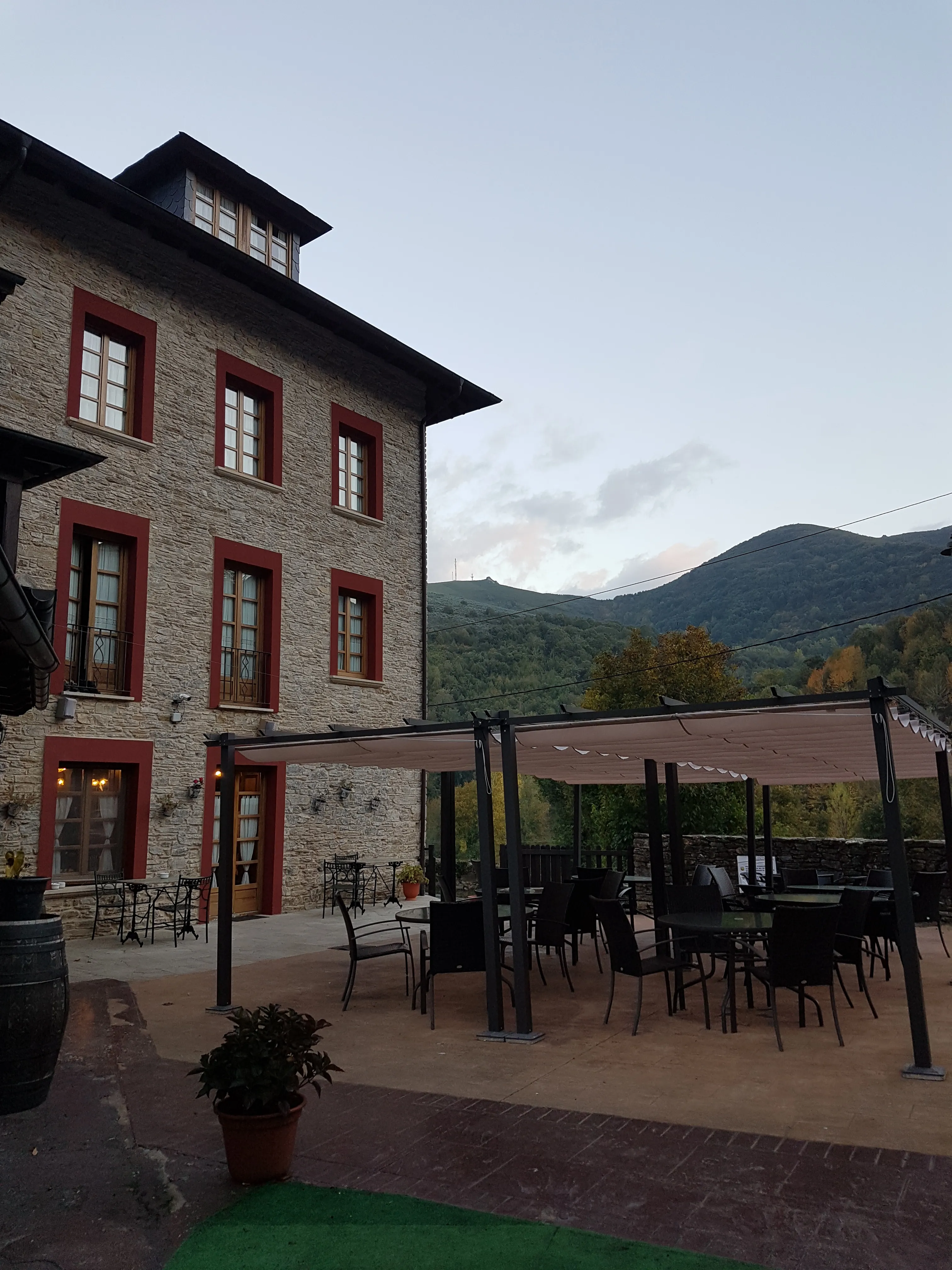 A stone Camino hotel with a terrace below wooded mountains.