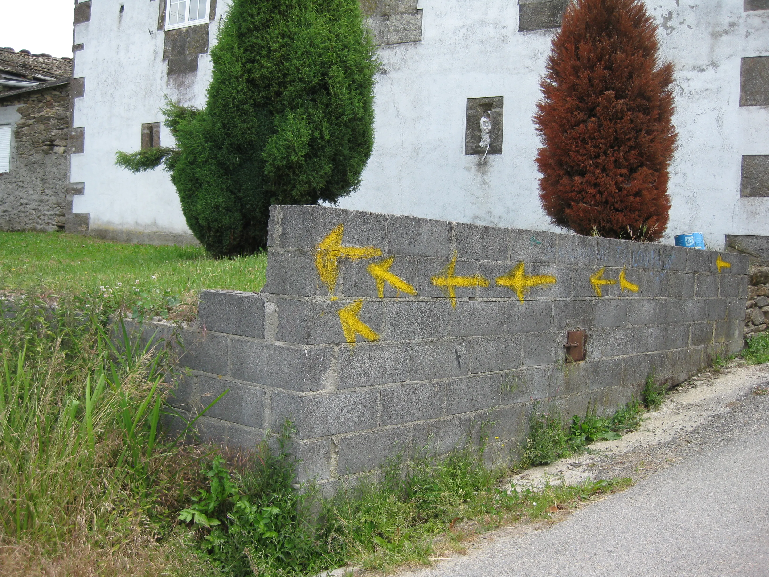 Several yellow Camino arrows painted in different directions on a village wall.