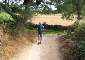 A pilgrim walking a rural Camino path with a light daypack.