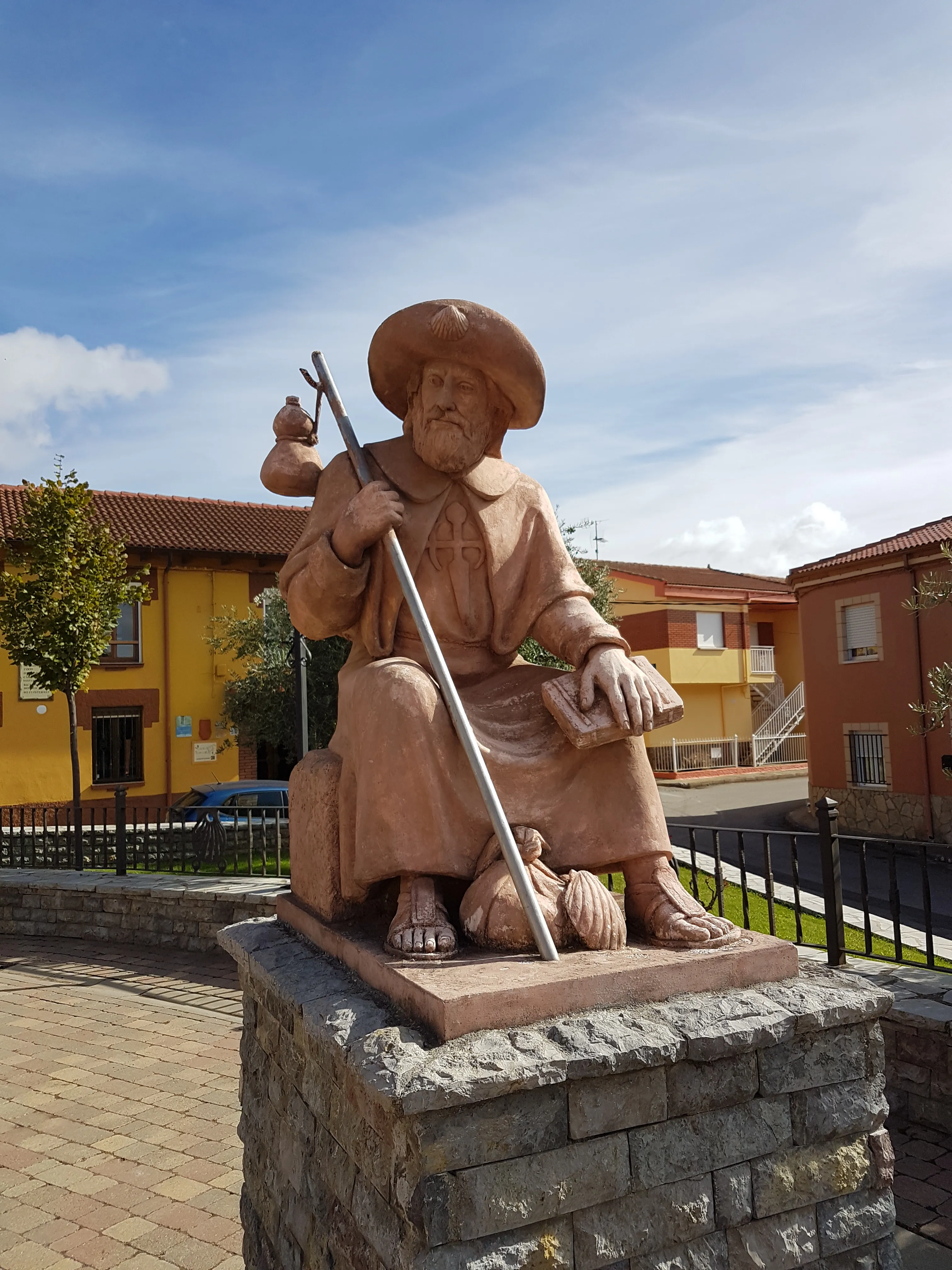 A seated pilgrim statue holding a staff and book beneath a blue sky.