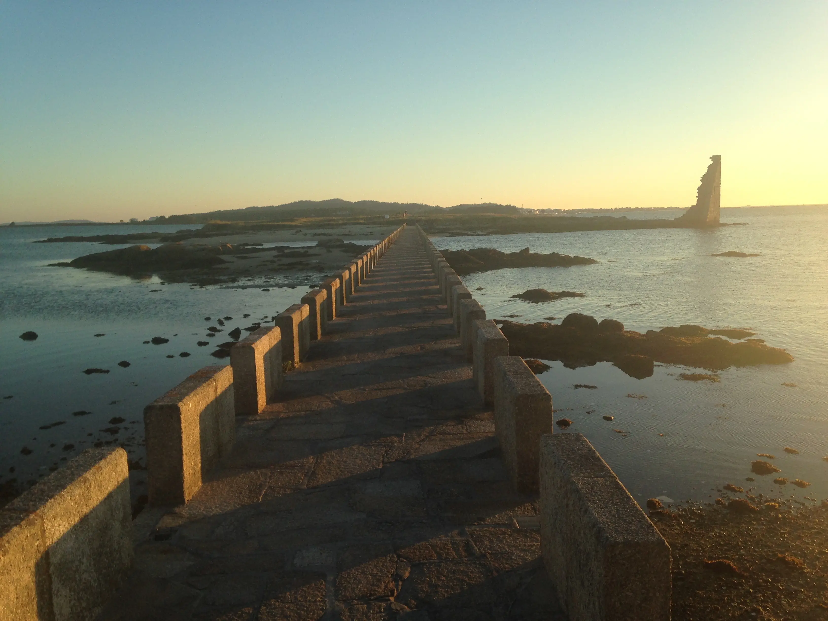 A stone walkway crossing the water in the Rías Baixas at sunset.