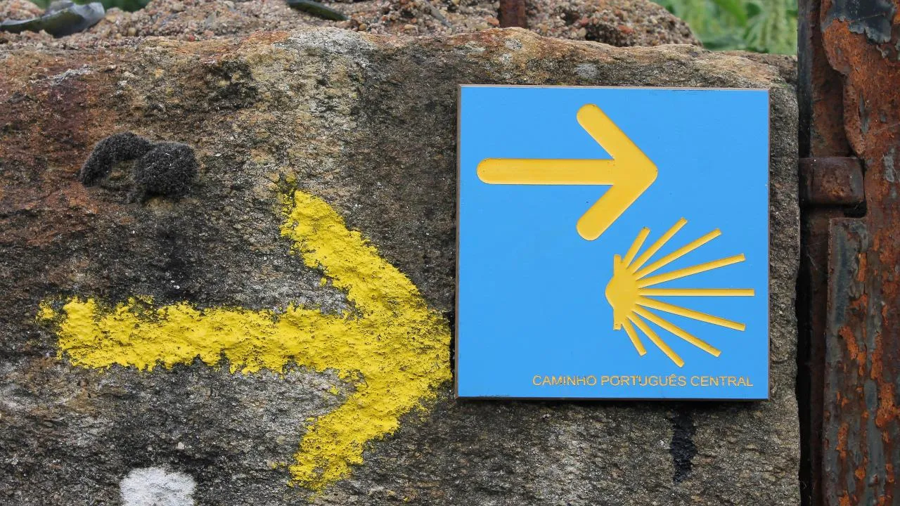 Yellow Camino arrows and a blue Camino Portugués waymarker on a stone wall.